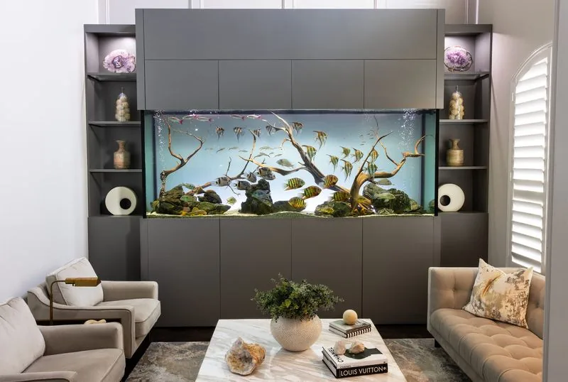 A driftwood aquascape in a freestanding aquarium beside a modern living room.