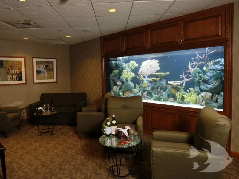 A reef aquarium framed by dark wood cabinetry in a reception lounge.
