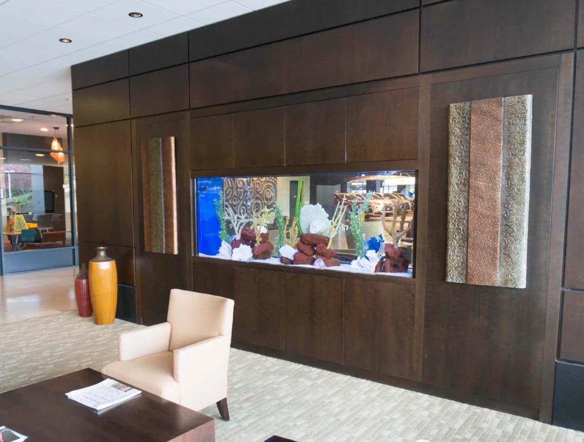 A reef aquarium set into dark wood panelling beside a reception seating area.