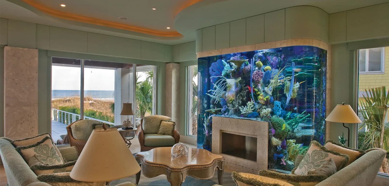A reef aquarium built into a sunlit living room with wide garden views.