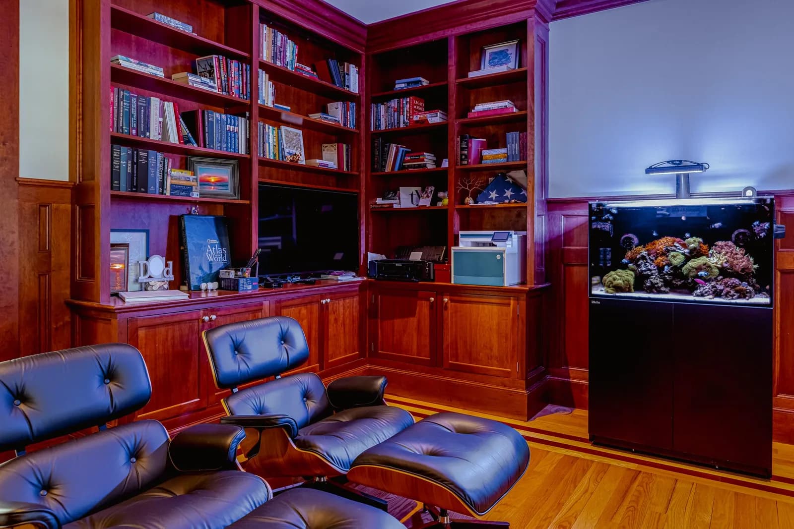 A reef aquarium integrated into dark wood bookshelves in a home library.